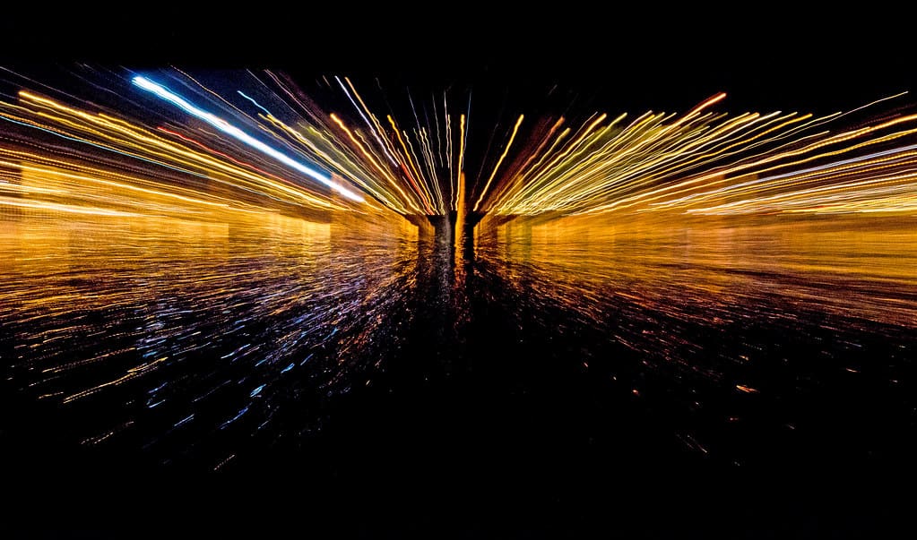 An abstract image of a "time warp": bright, wavy lines of yellow light burst over a dark space, perhaps the ocean.