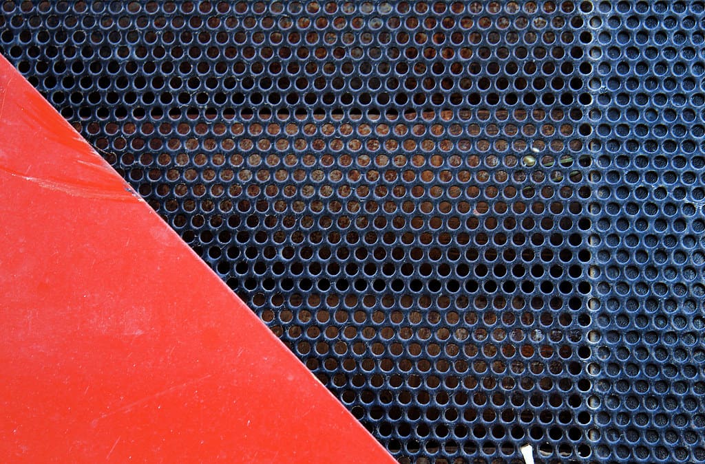 An image of a metal grate with a red triangle in the bottom left corner.